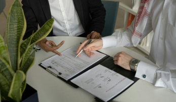 two men sitting at a table with papers and a pen